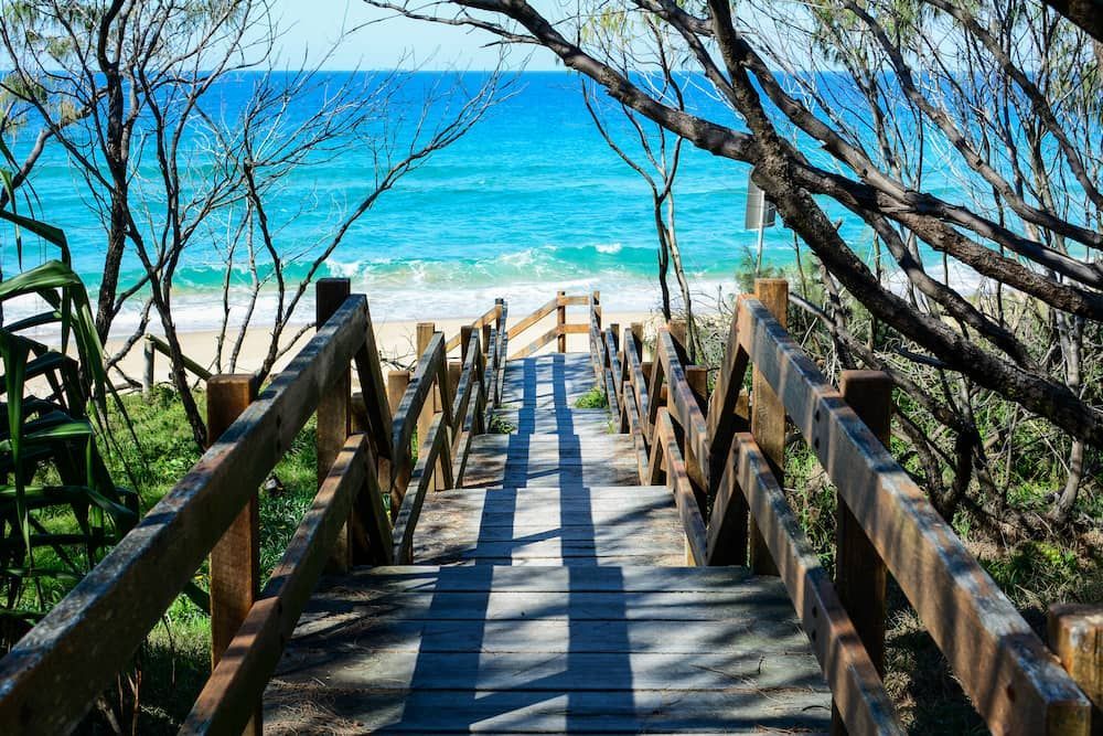 A Wooden Walkway Leading to the Beach With a View of the Ocean — We Clean Lounges In Mooloolaba, QLD