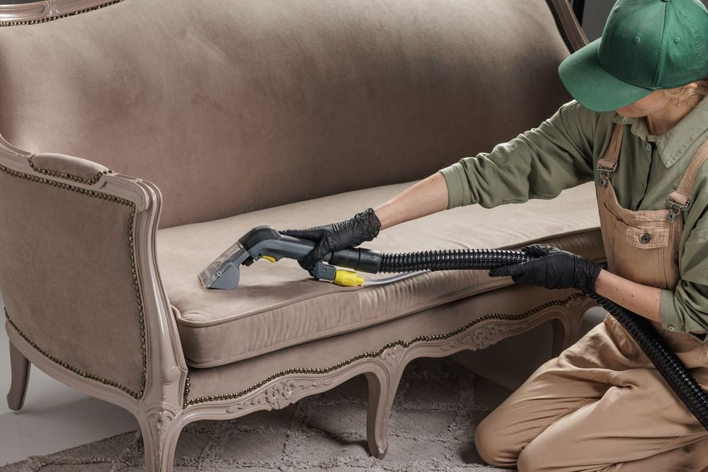 A Person Wearing a Green Cap and Beige Overalls Uses a Vacuum Tool — We Clean Lounges In Palmview, QLD