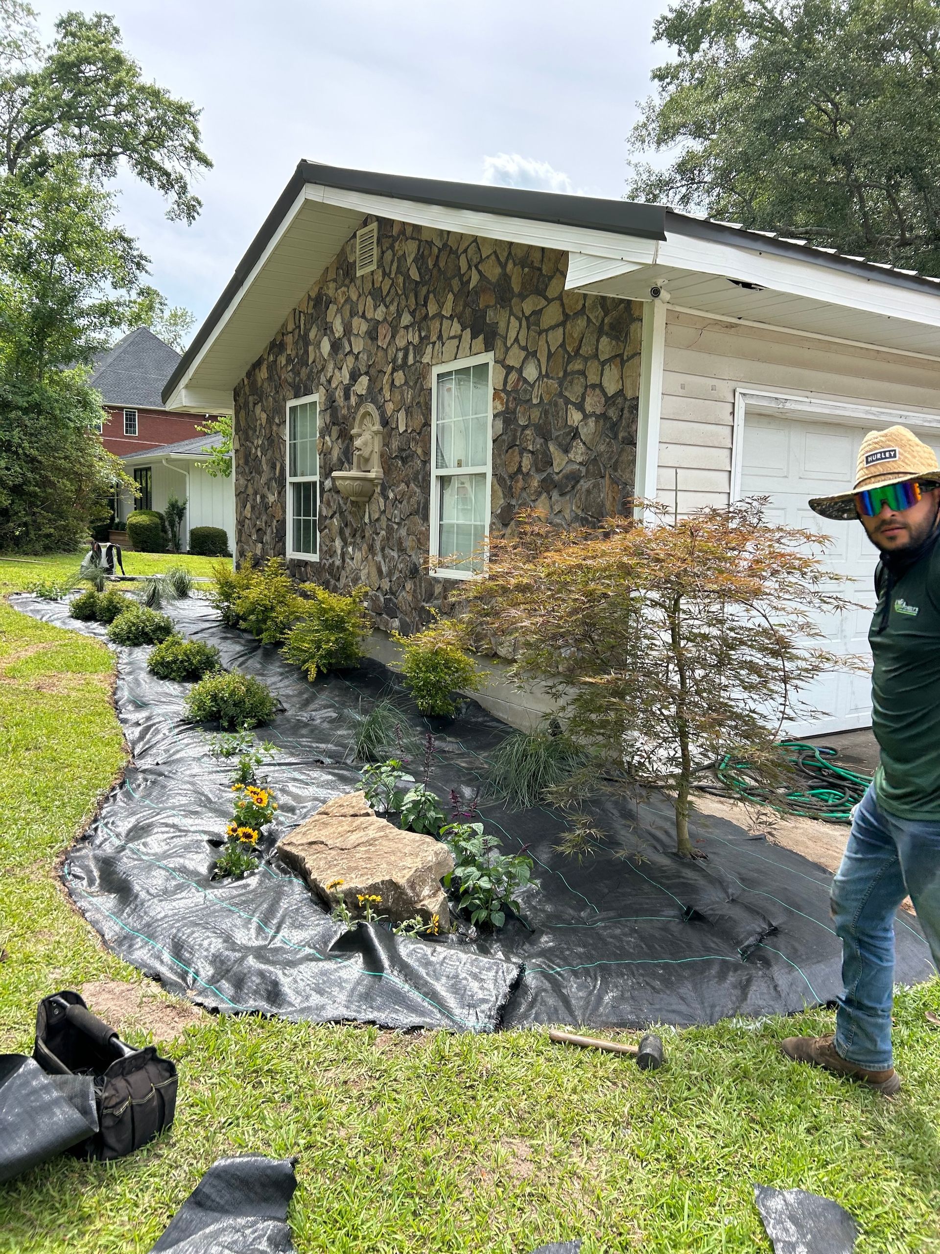 Landscaped house side yard with fresh mulch, shrubs, and a man standing near the wall