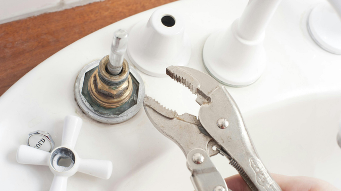 Hand using pliers to loosen a faucet part on a white sink.