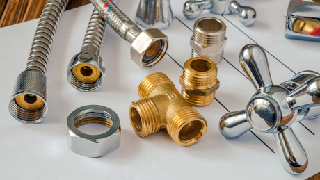 Plumbing parts arranged on a blueprint: chrome and brass fixtures, flexible hoses, nuts, valves.