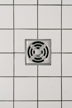 Square shower drain in white tiled floor.