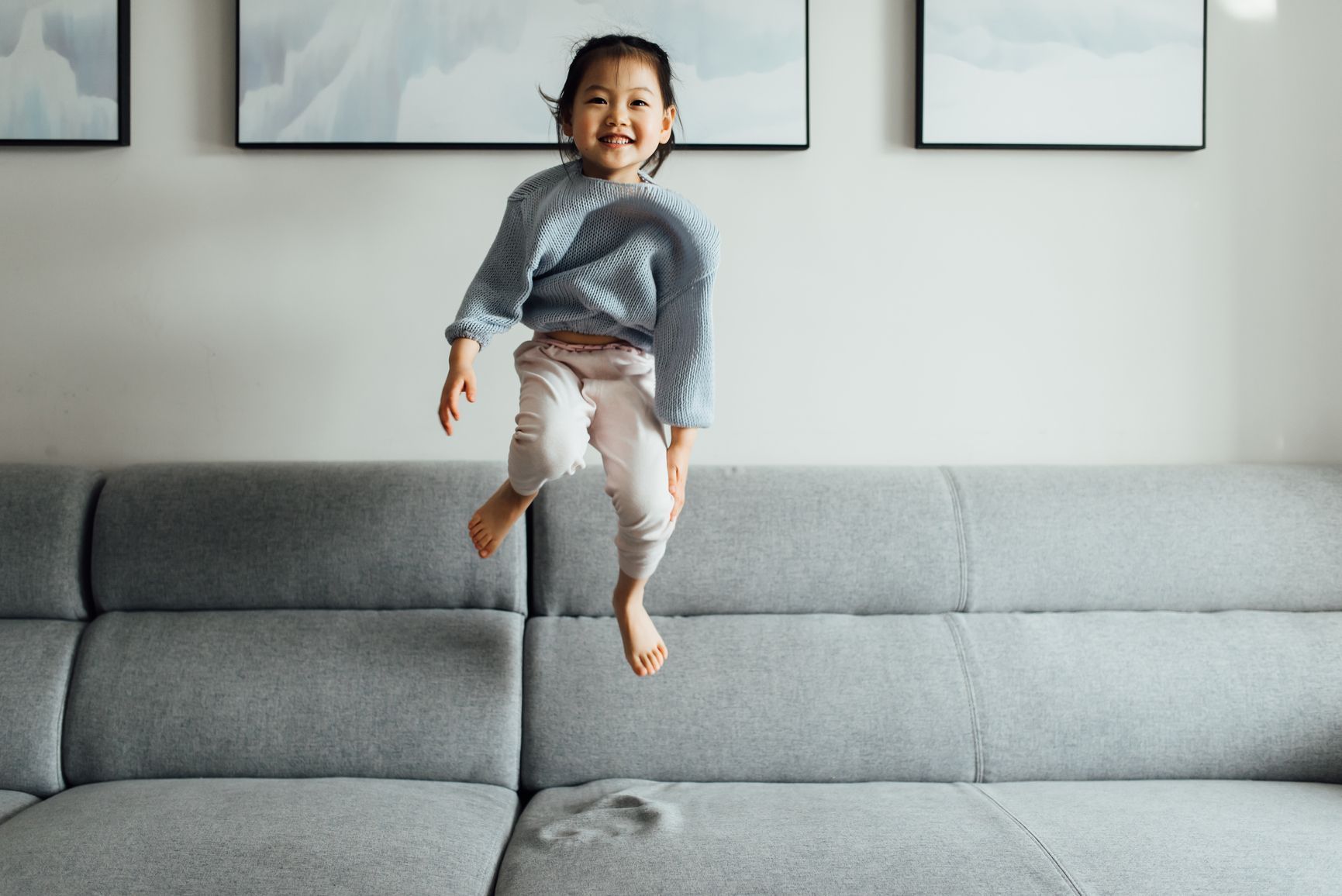A little girl is jumping in the air while sitting on a couch.