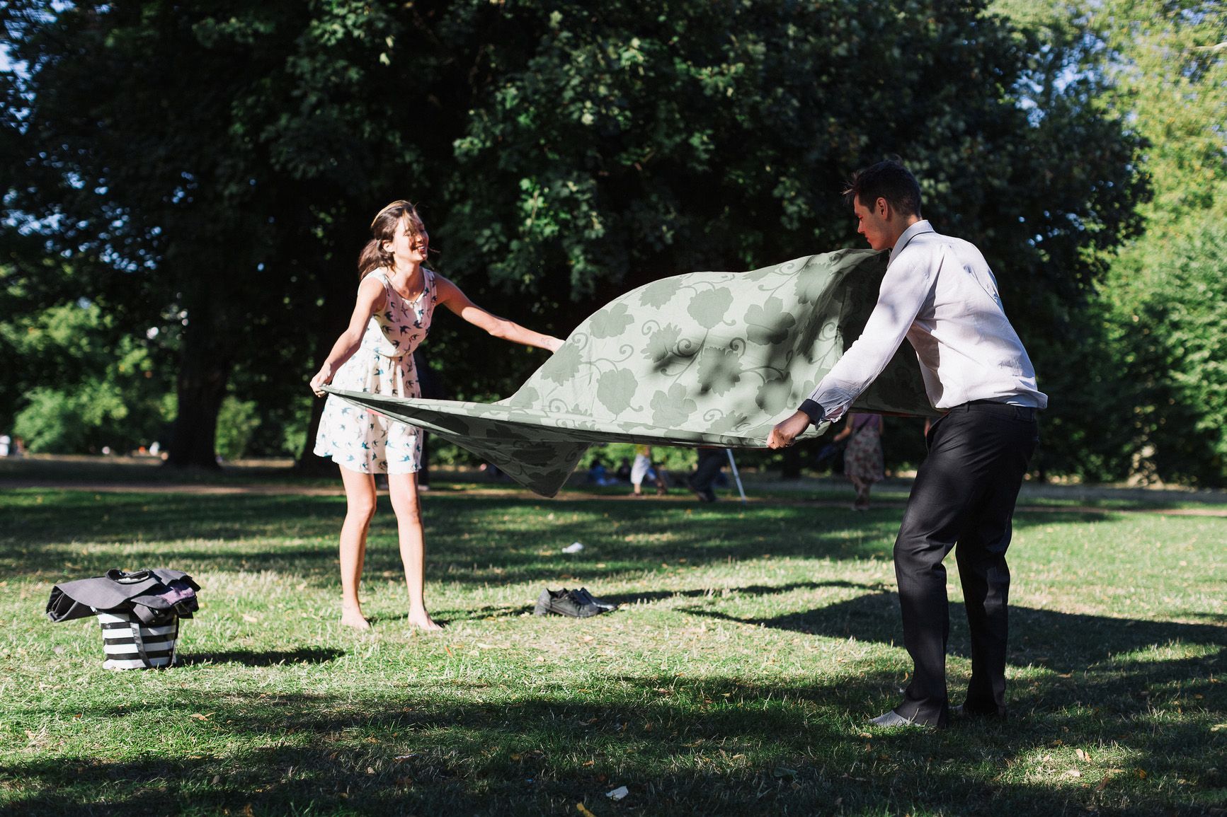 A man and a woman are playing with a blanket in a park