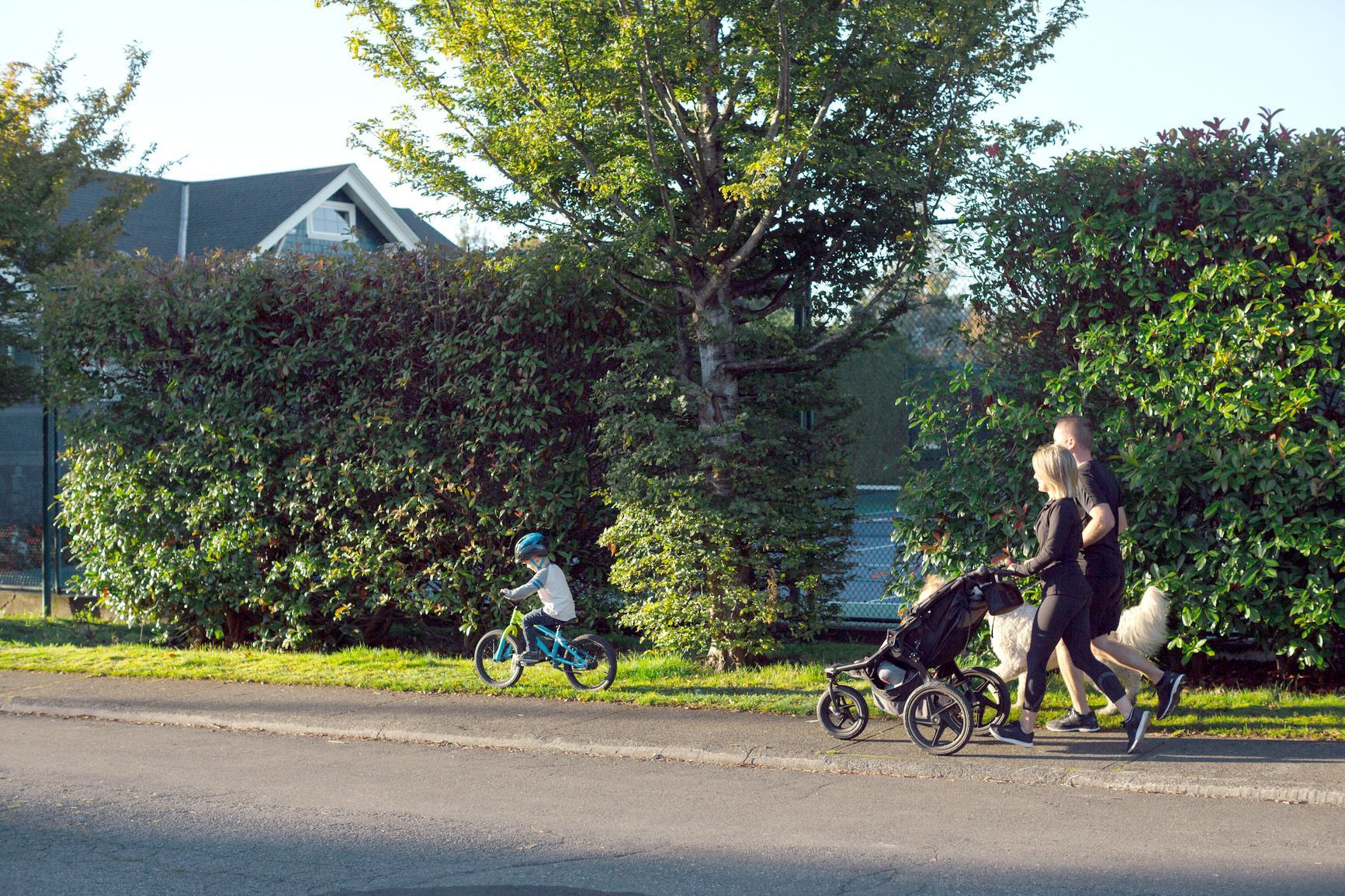 A family is walking down the street with a stroller and a child riding a bike.