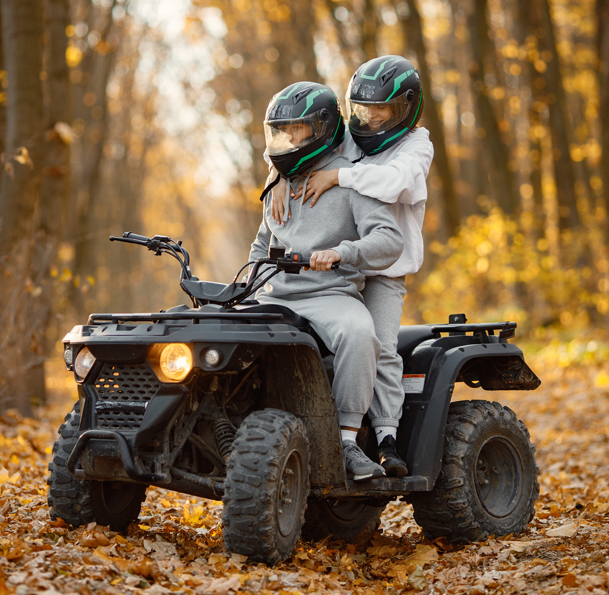 A man and a woman are riding an atv in the woods.