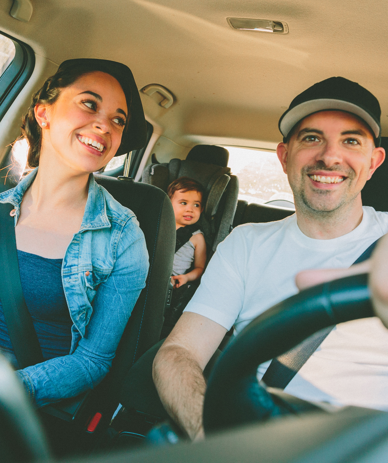 A man and woman are driving a car with a child in the back seat