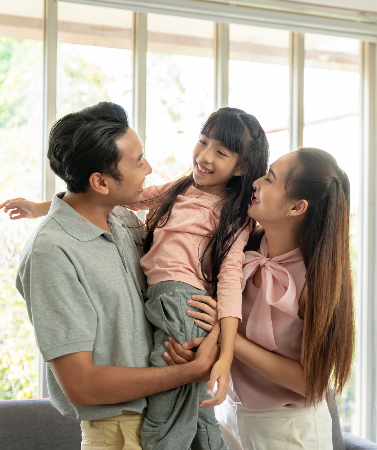 A man and woman are holding a little girl in their arms in a living room.