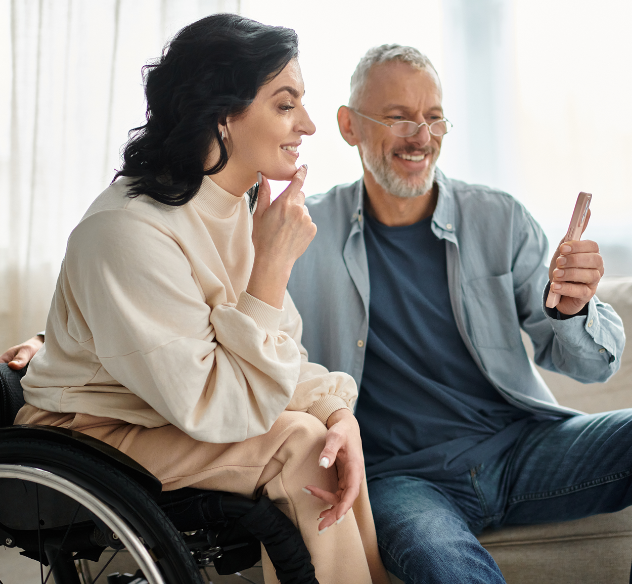 A woman in a wheelchair is sitting next to a man on a couch.