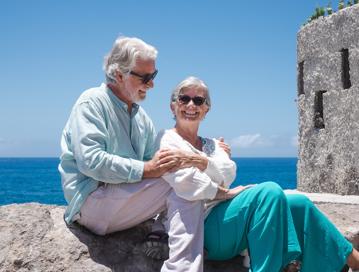 An elderly couple is sitting on a rock overlooking the ocean.