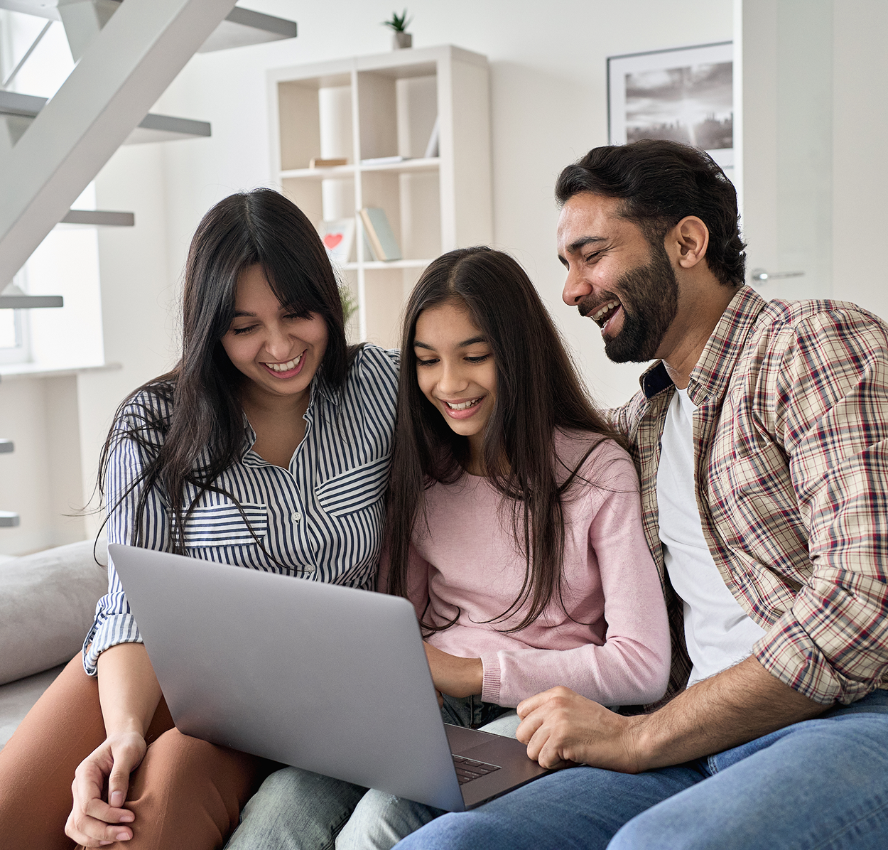 A family is sitting on a couch looking at a laptop computer.