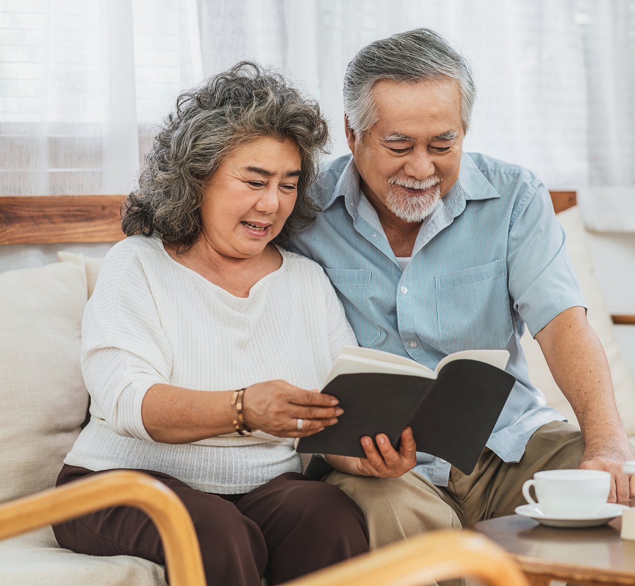 A man and a woman are sitting on a couch reading a book.
