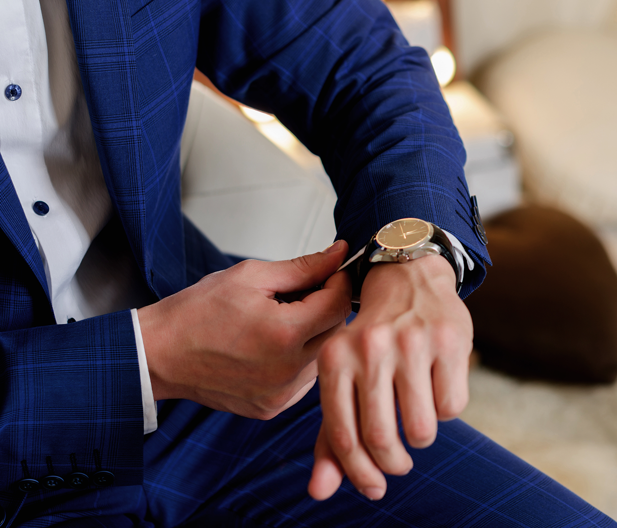 A man in a blue suit is adjusting his watch