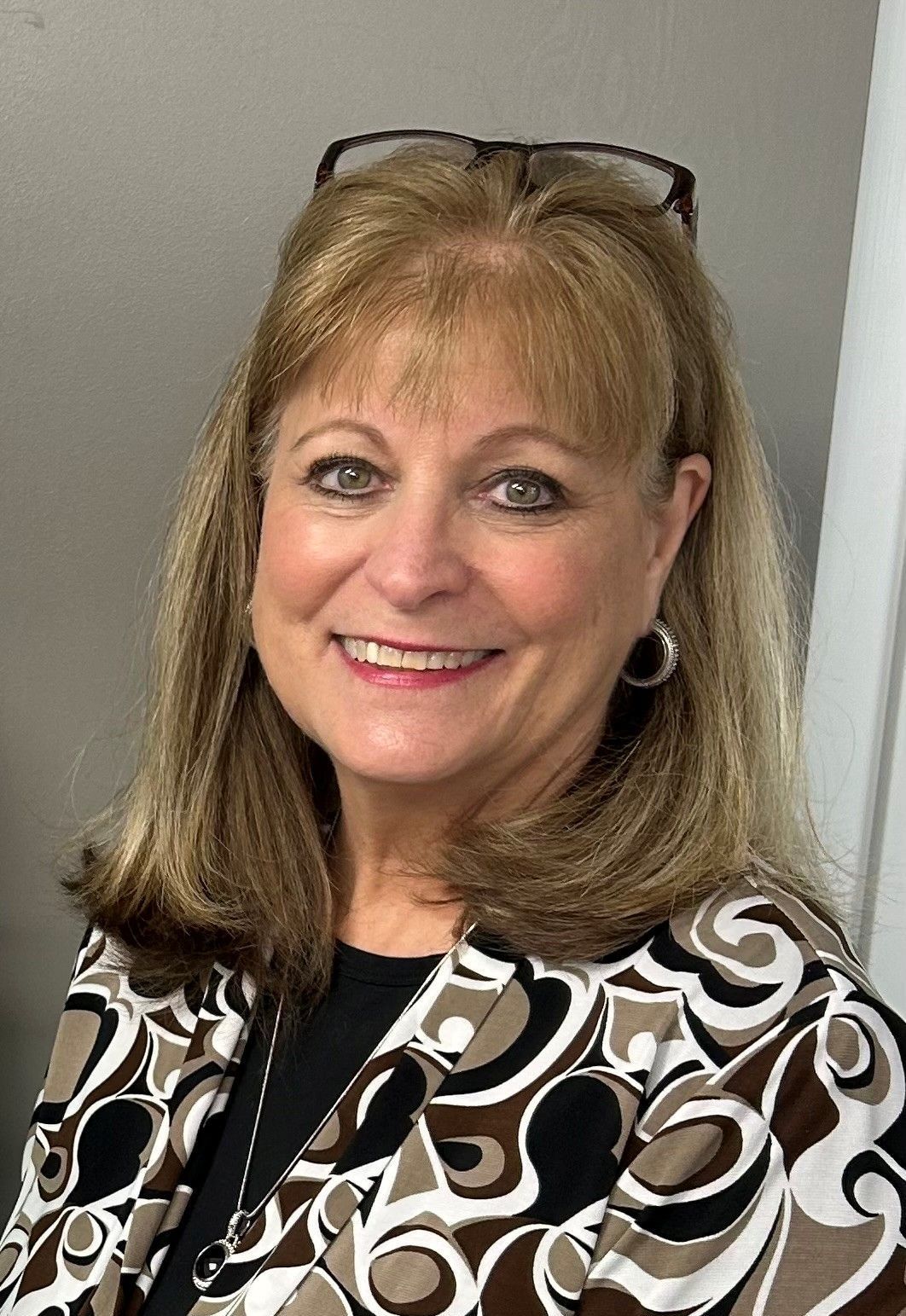 A woman wearing glasses and a jacket is smiling for the camera.