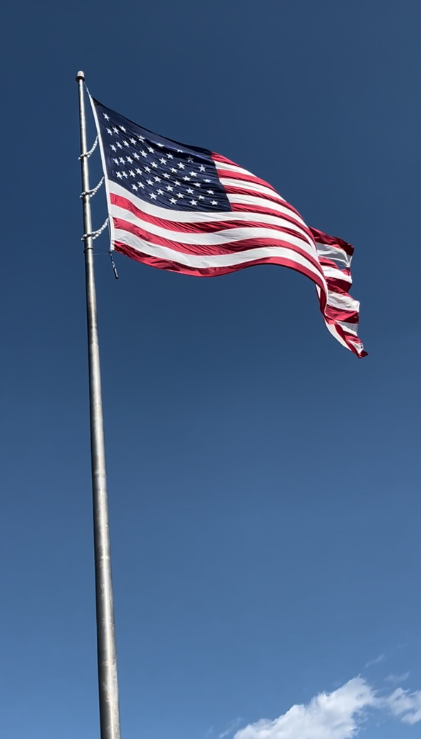 An american flag is waving in the wind against a blue sky.