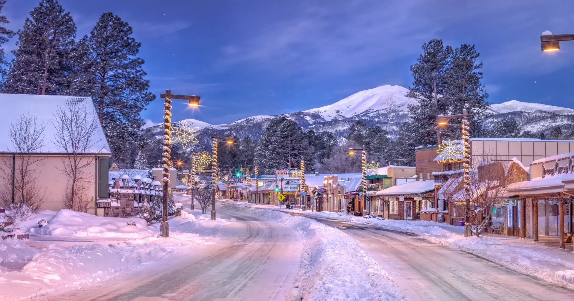 A snowy street in a small town with a mountain in the background.