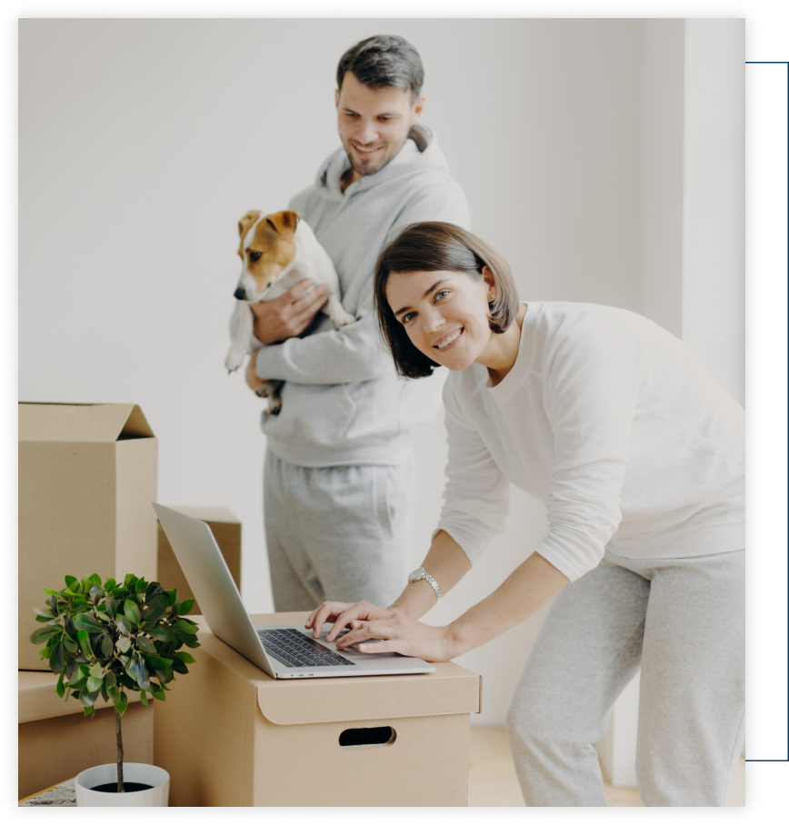 A woman is using a laptop while a man holds a dog