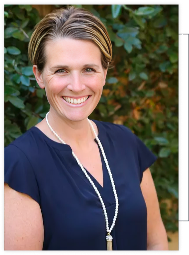A woman wearing a blue shirt and a pearl necklace is smiling.