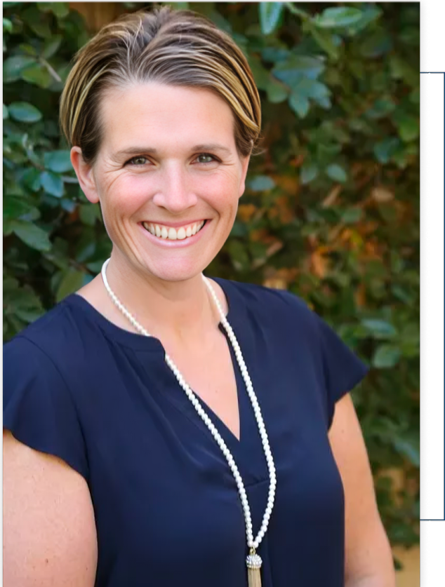 A woman wearing a blue shirt and a pearl necklace is smiling.