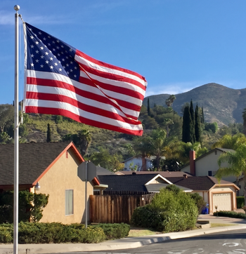 American flag waving over suburban homes with mountains in the background