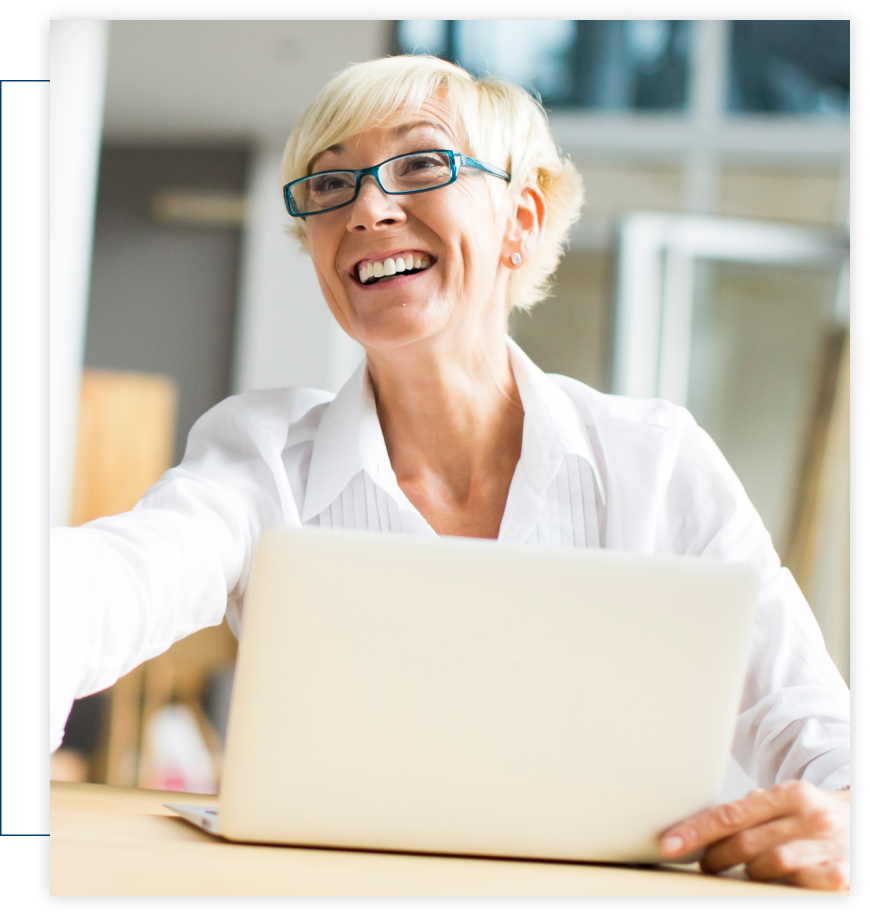 A woman wearing glasses is smiling while using a laptop computer