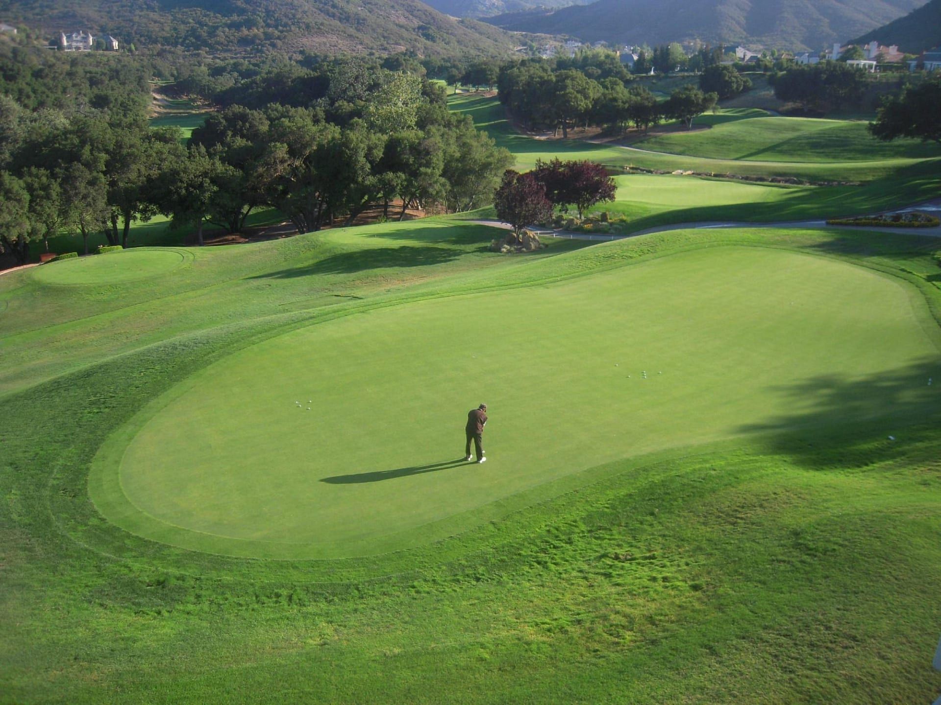 A man is standing on the green of a golf course.