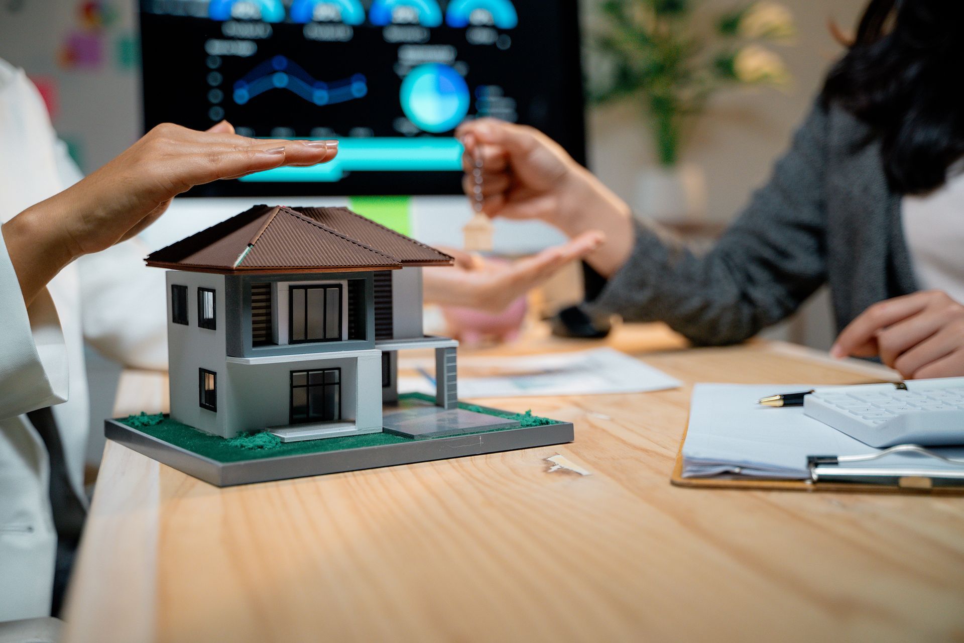 A woman is giving a key to another woman in front of a model house.