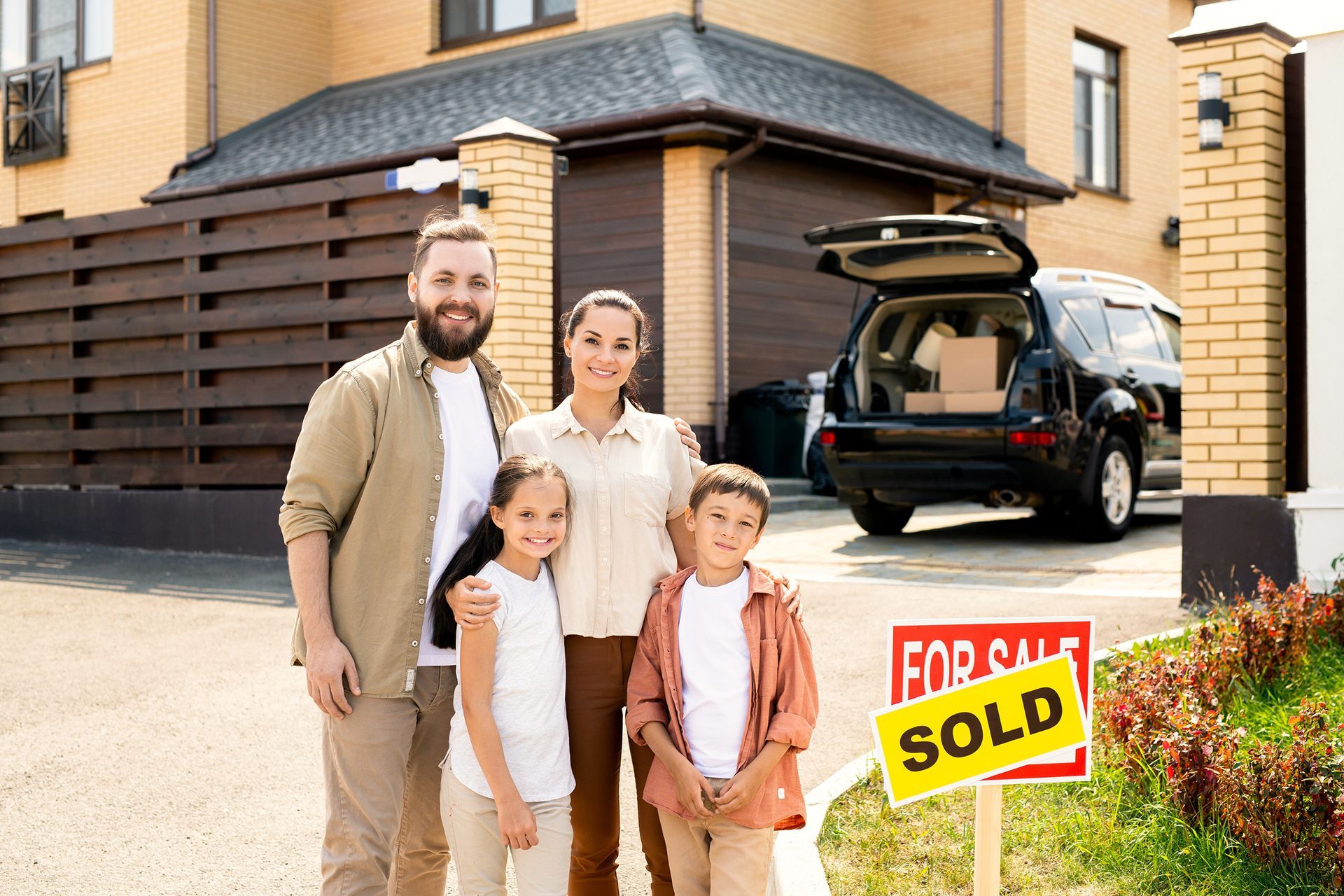A family is standing in front of a for sale sign in front of their new house.