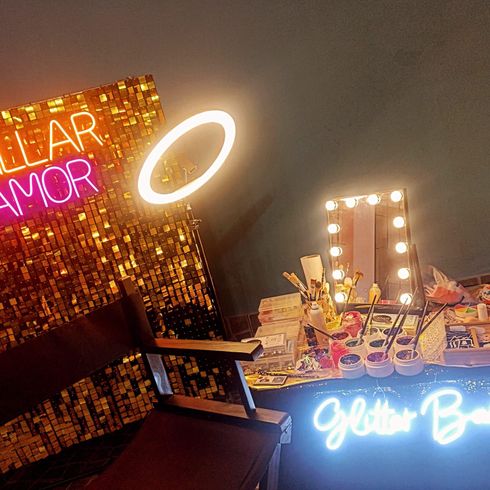 Un bar con purpurina, decorado con un letrero de neón, un espejo de tocador iluminado y un aro de luz .