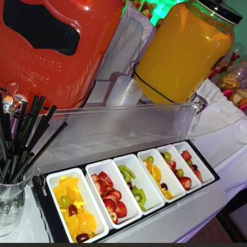 Una estación de bebidas y guarniciones de fruta con dispensadores de zumo de naranja.