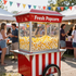 Un carrito de palomitas de maíz de color rojo brillante se encuentra en un evento festivo al aire libre, lleno de palomitas.