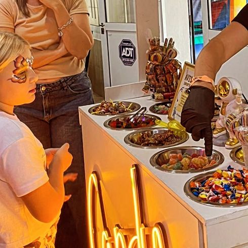 Una persona con un guante negro coge caramelos de una hilera de cuencos metálicos .