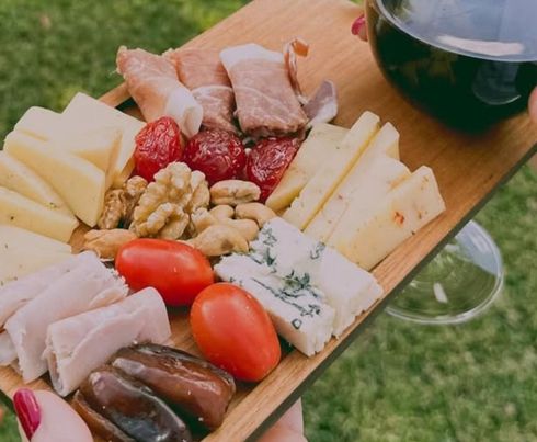 Una tabla de madera contiene una selección de quesos, embutidos, frutos secos,etc.