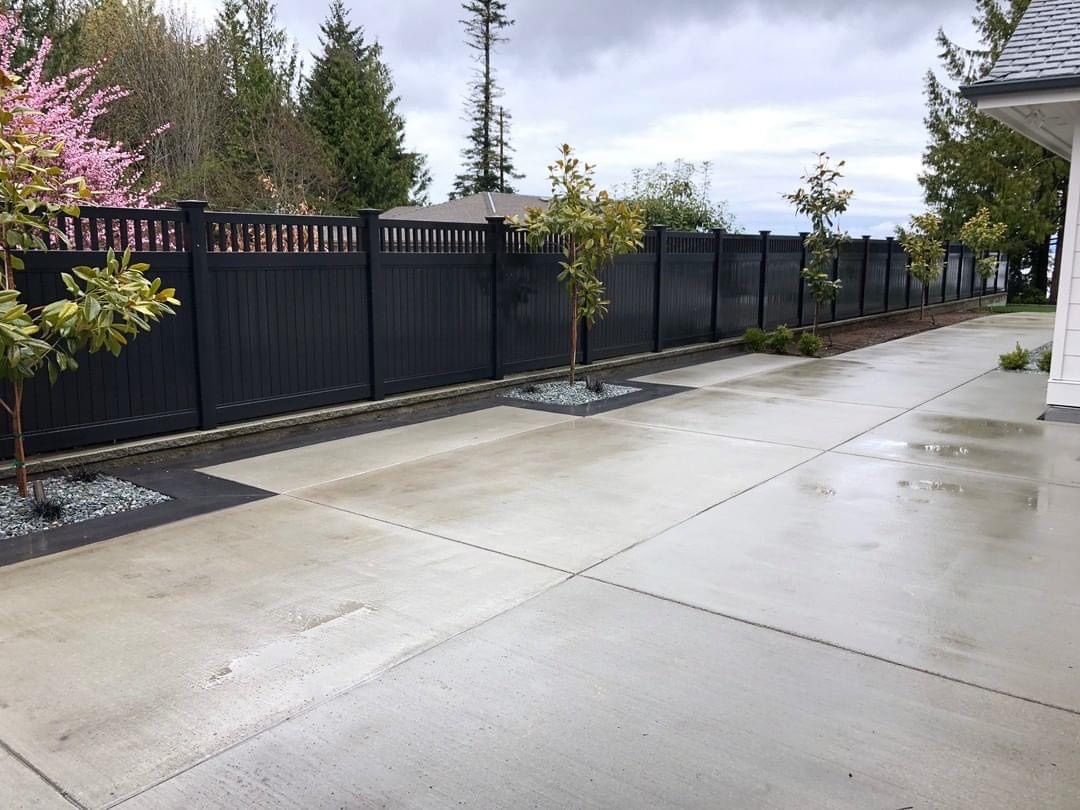 A black fence surrounds a concrete driveway in front of a house.
