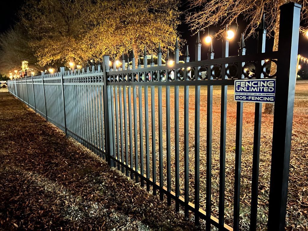 A long metal fence is lit up at night in a park.
