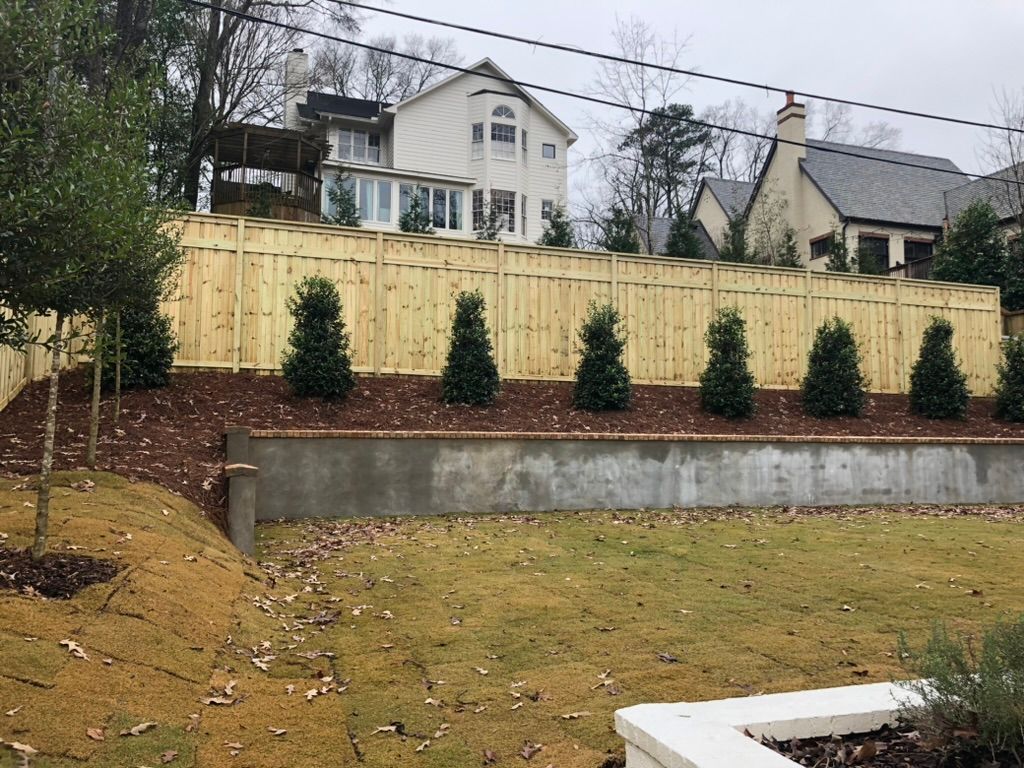 A wooden fence surrounds a large swimming pool in a backyard.
