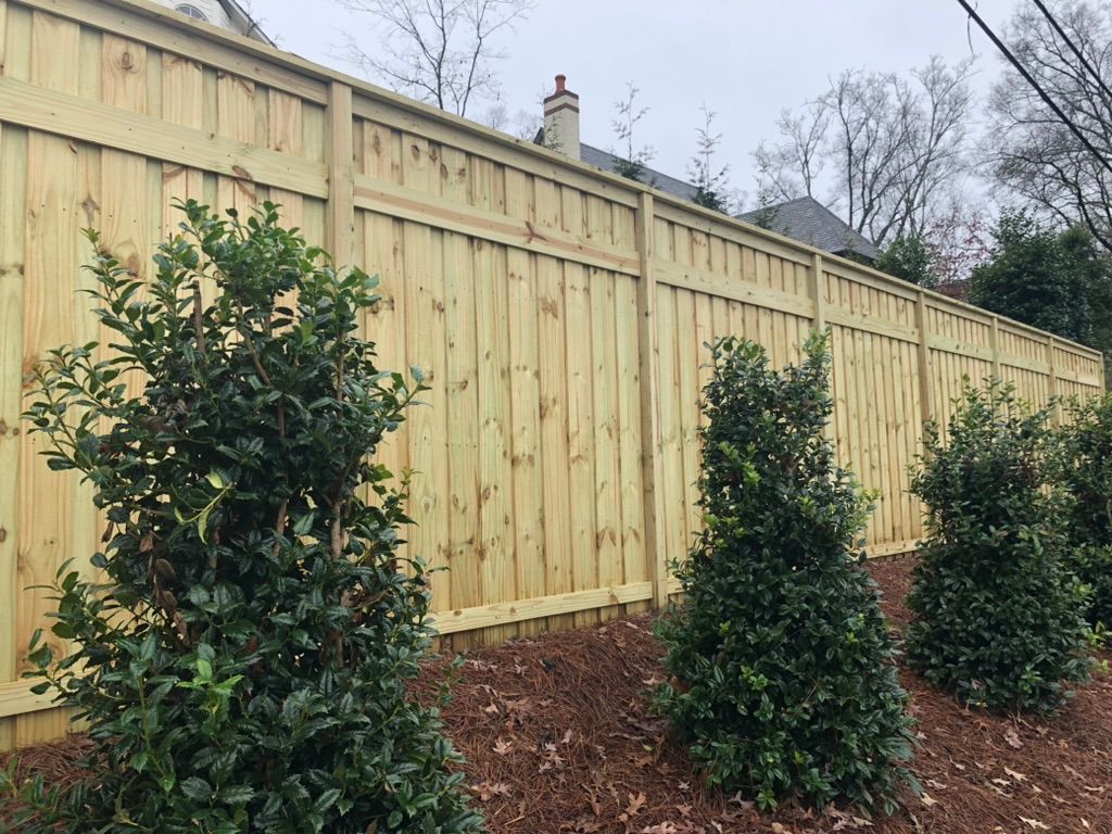 A wooden fence surrounded by trees and bushes in a yard.