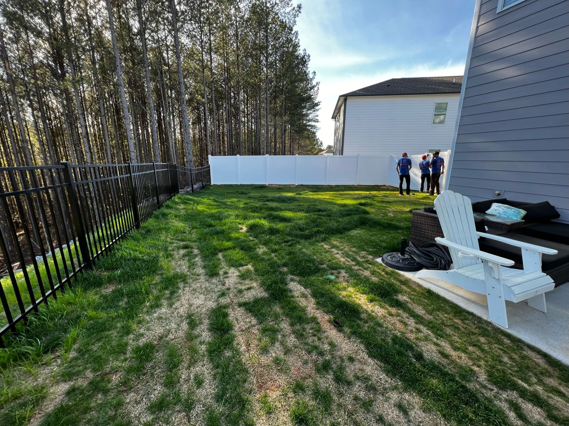 A group of people are standing in a backyard with a white fence.