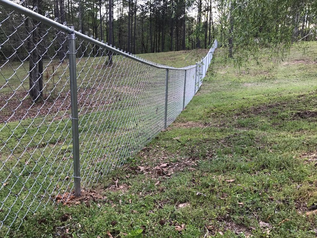 A chain link fence is sitting in the middle of a grassy field.