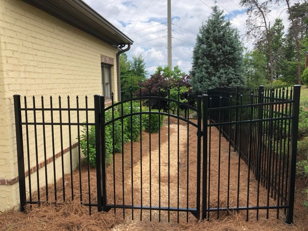 A black wrought iron fence with a gate in front of a yellow brick house.