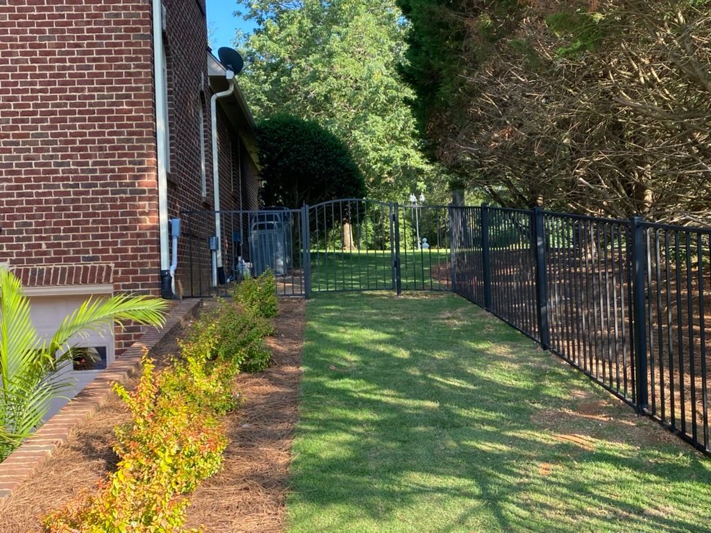 A brick house with a fence around it and a lush green yard.