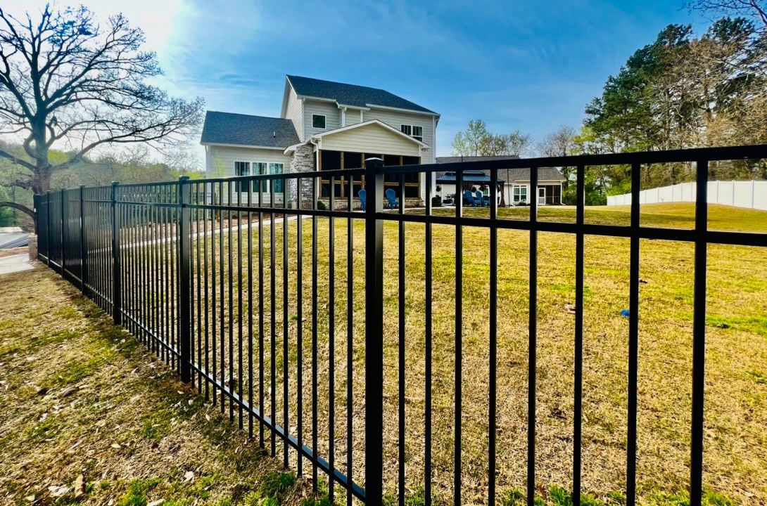 A black metal fence surrounds a grassy field in front of a house.