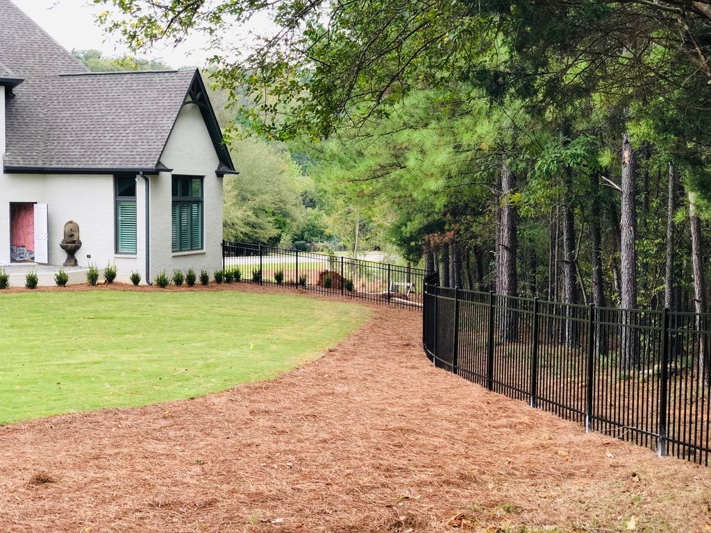 A white house with a black fence in front of it is surrounded by trees.