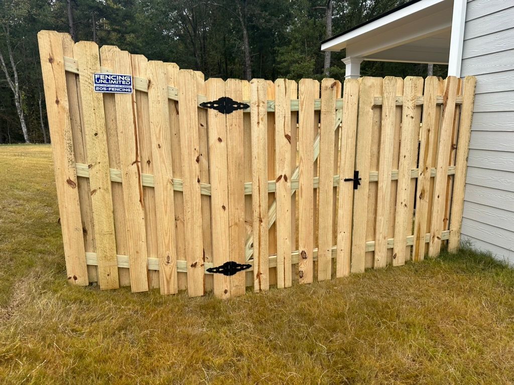 A wooden fence is sitting in the grass next to a house.