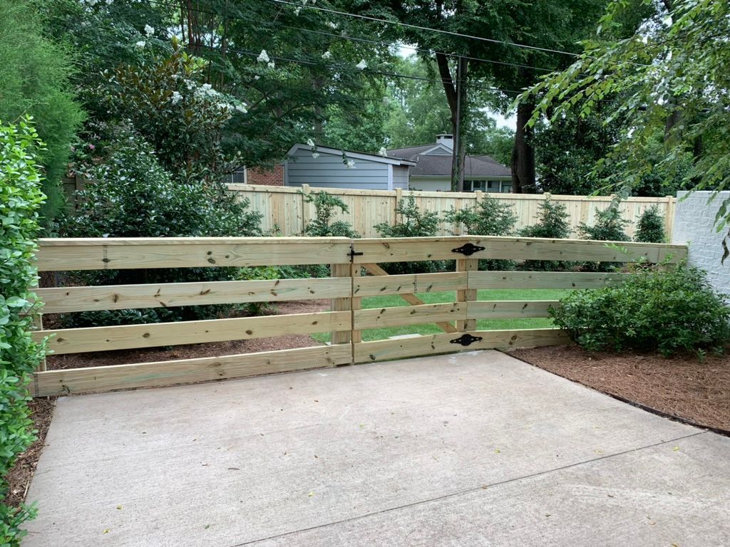 A wooden fence surrounds a driveway with trees in the background