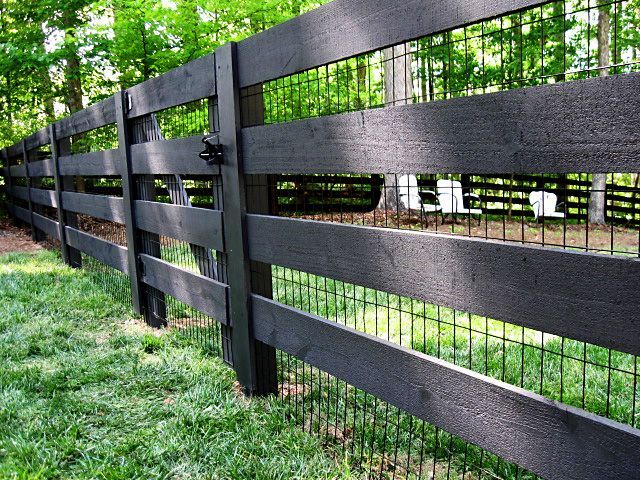 A black wooden fence with a wire fence behind it