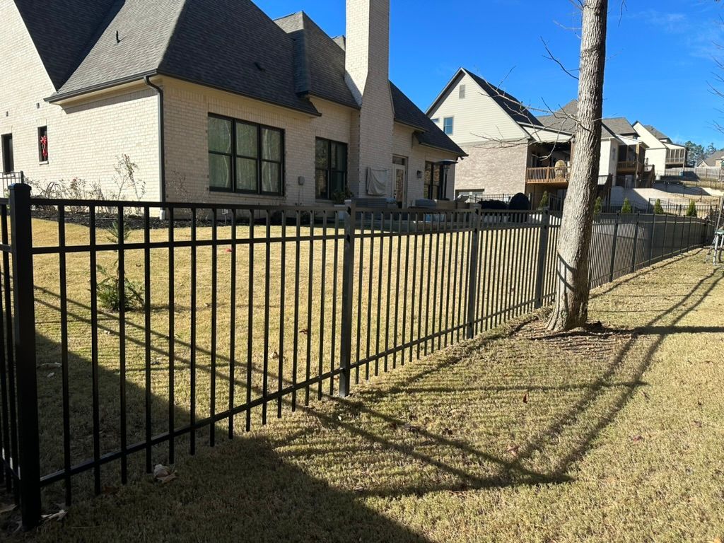 A black metal fence surrounds a large house in a residential area.