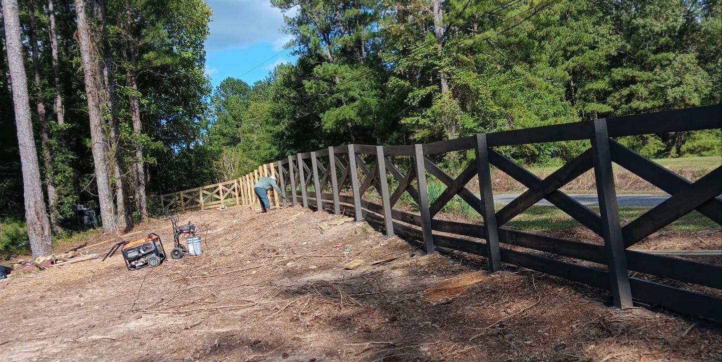 A wooden fence surrounds a dirt road in the middle of a forest.