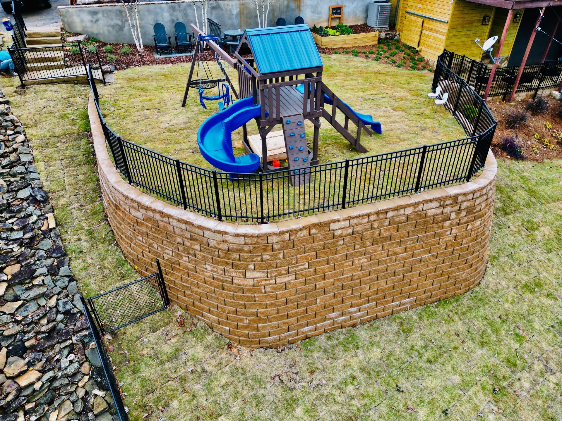 An aerial view of a playground in a backyard behind a brick wall.