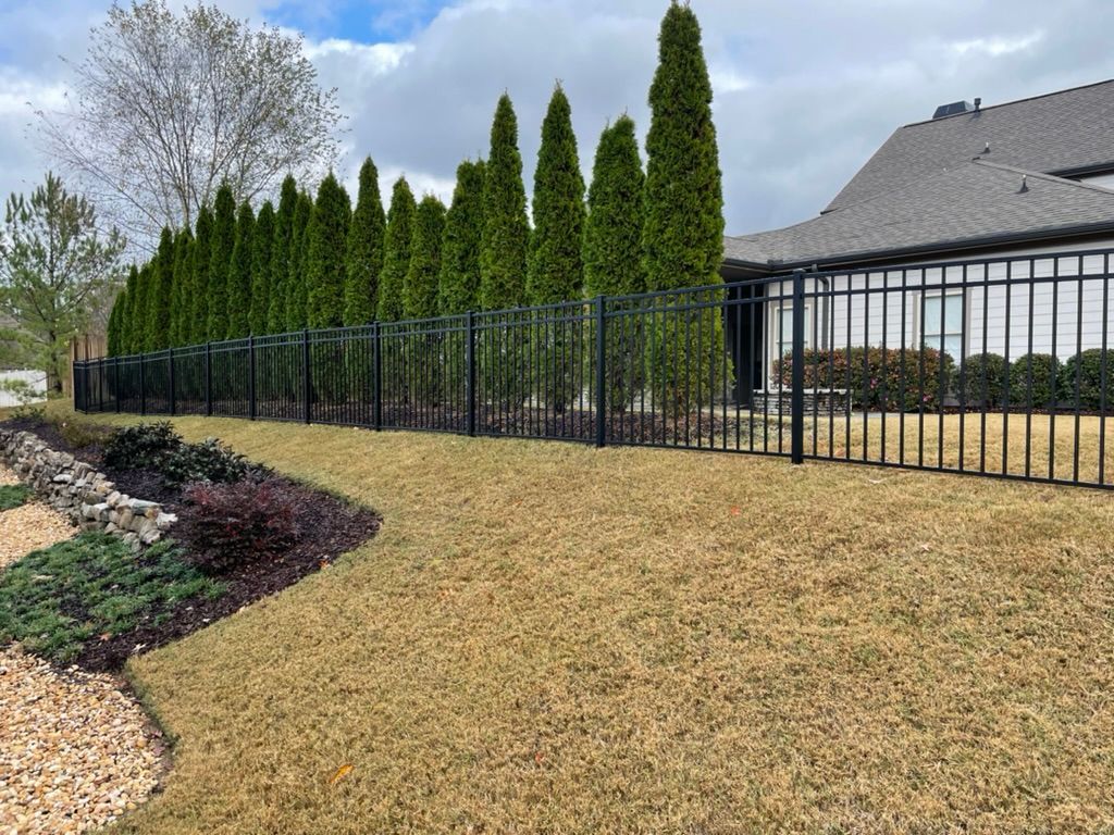 A metal fence surrounds a lush green yard in front of a house.